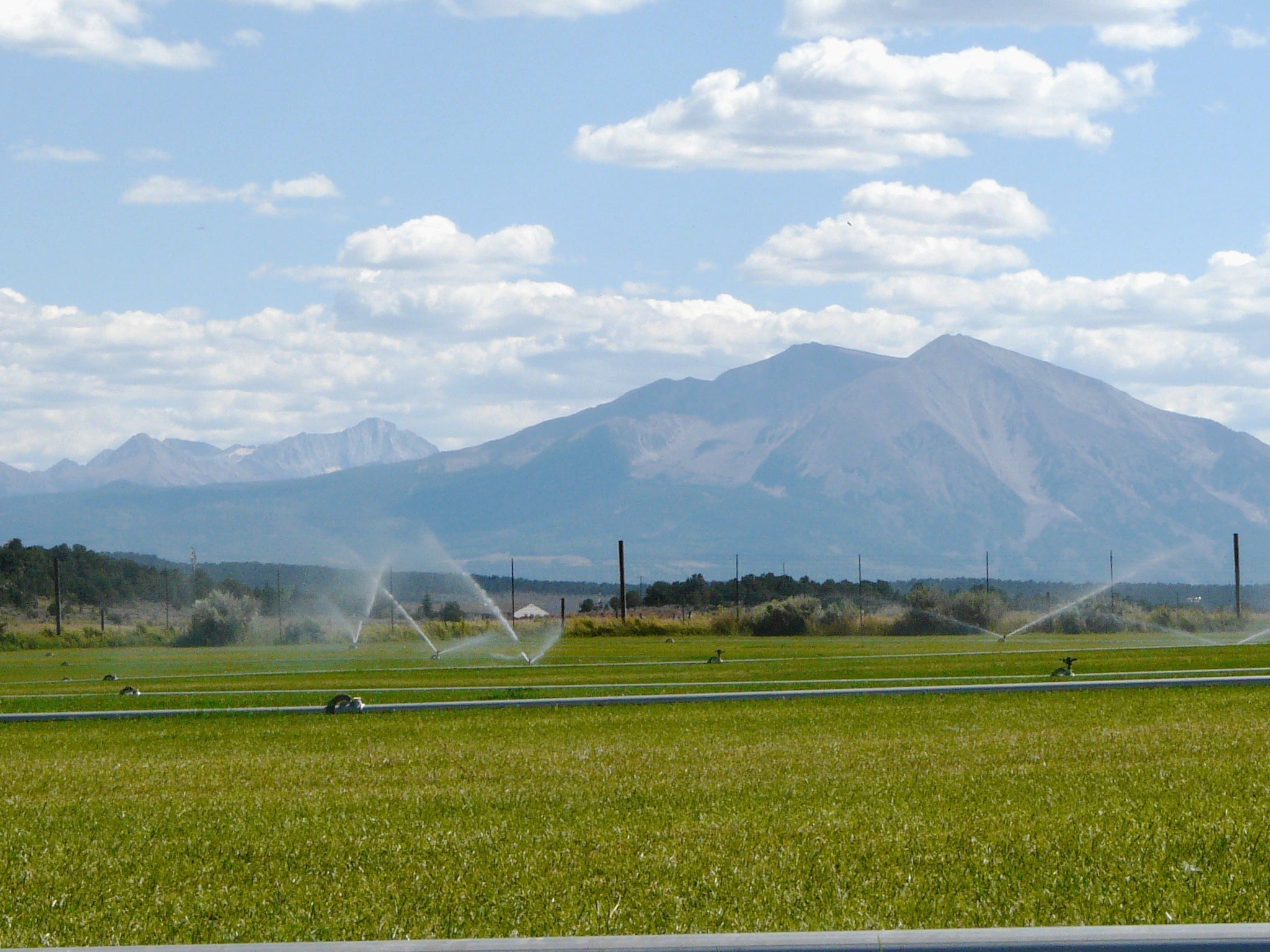 Irrigated farmland with mountain backdrop under a partly cloudy sky.