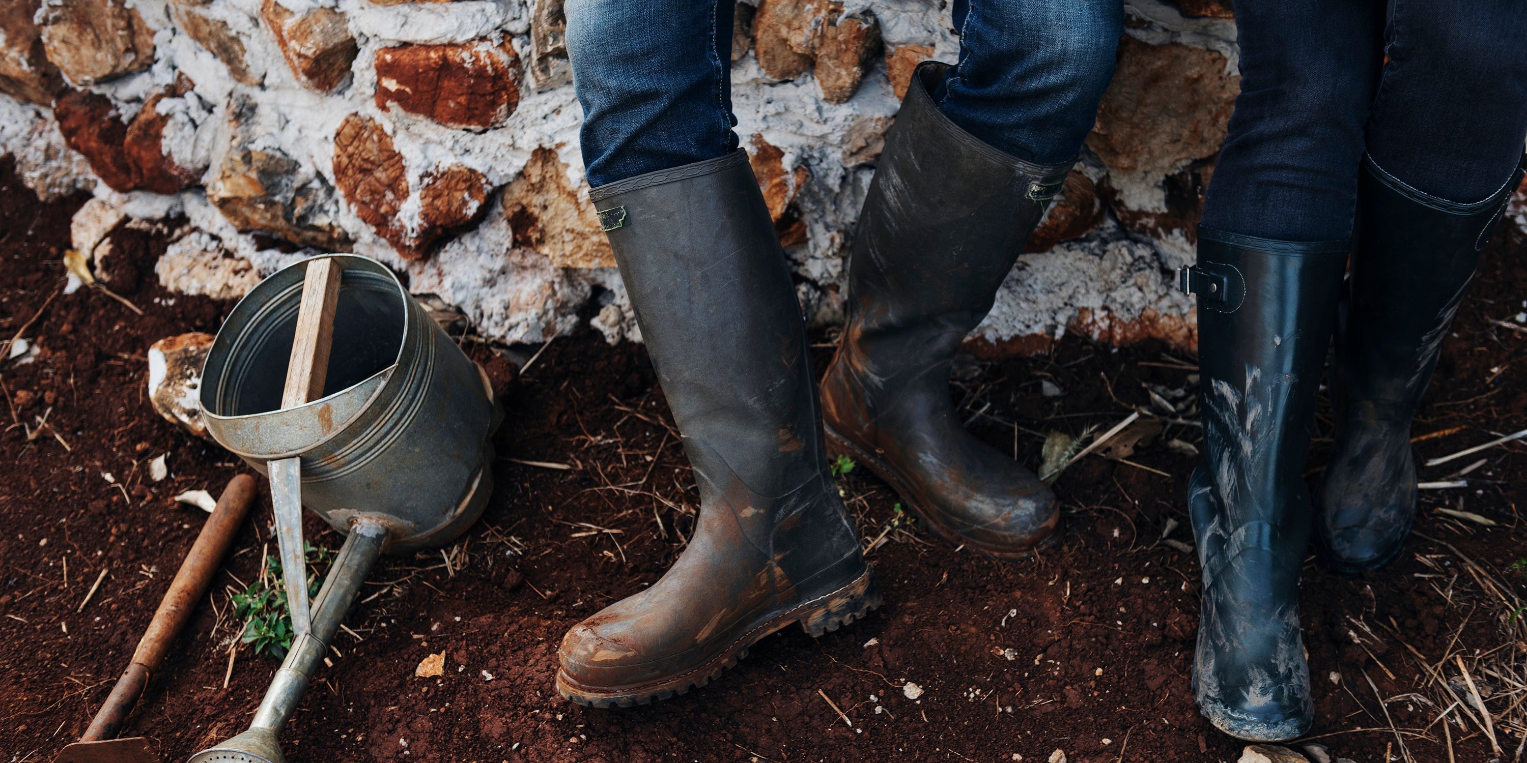 Rubber boots and a metal watering can standing on freshly turned garden soil