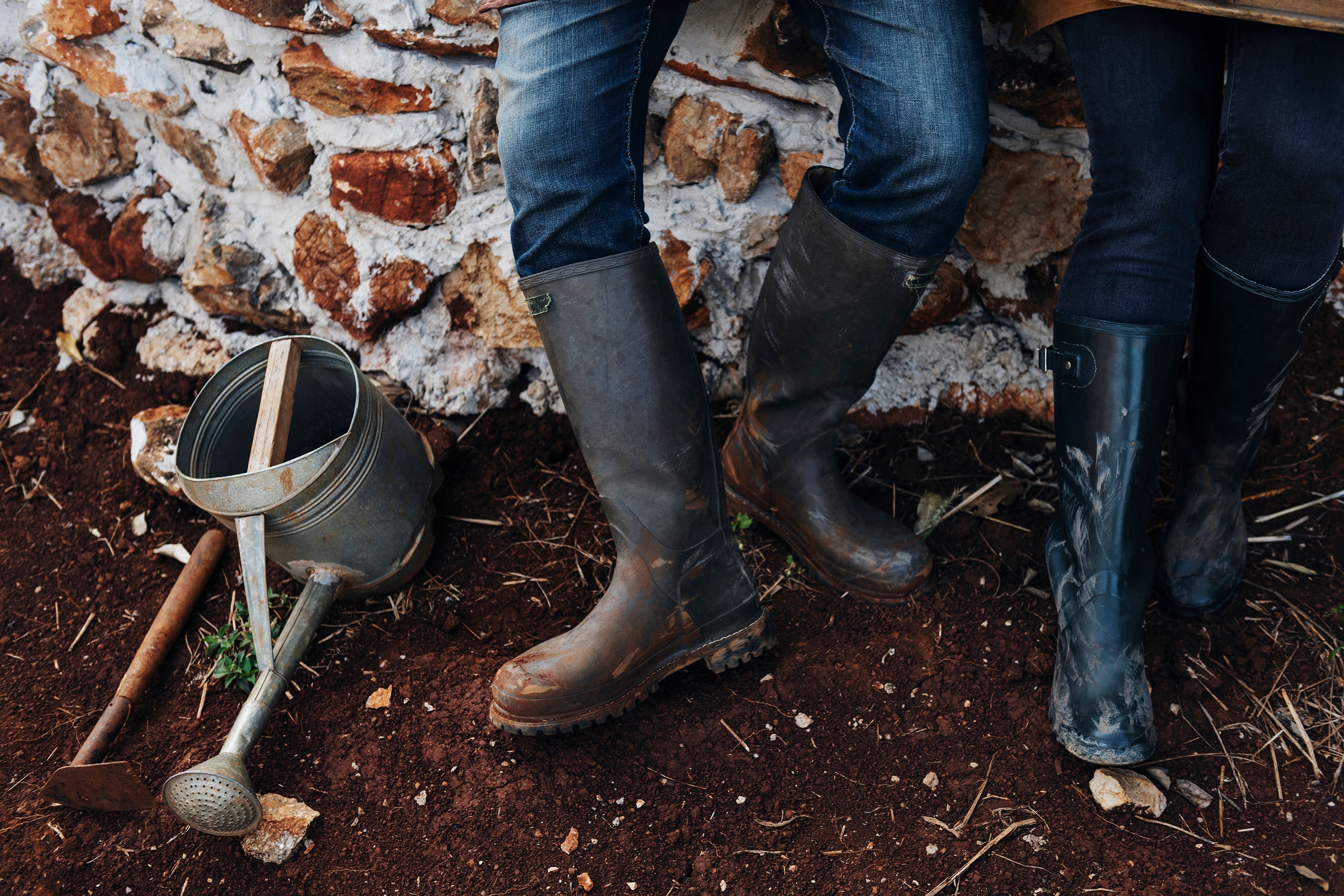 Rubber boots and a metal watering can standing on freshly turned garden soil