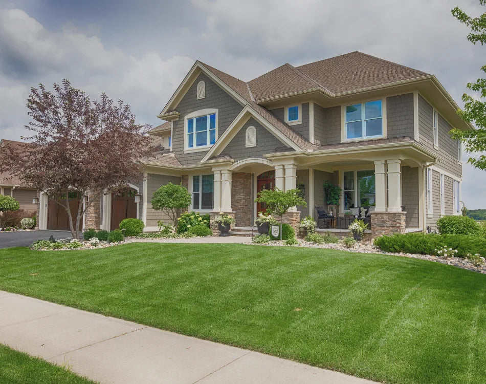 Two-story suburban home with manicured striped front lawn and foundation landscaping under a cloudy sky.