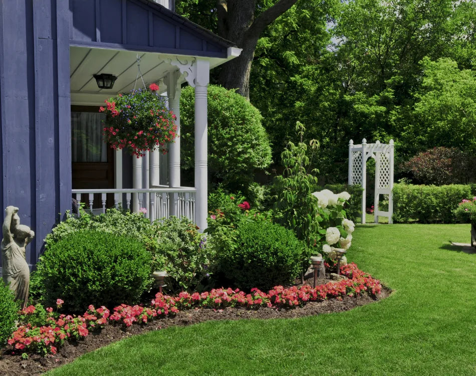 Front porch garden design with red impatiens, boxwoods, hanging baskets, and a white lattice arbor.