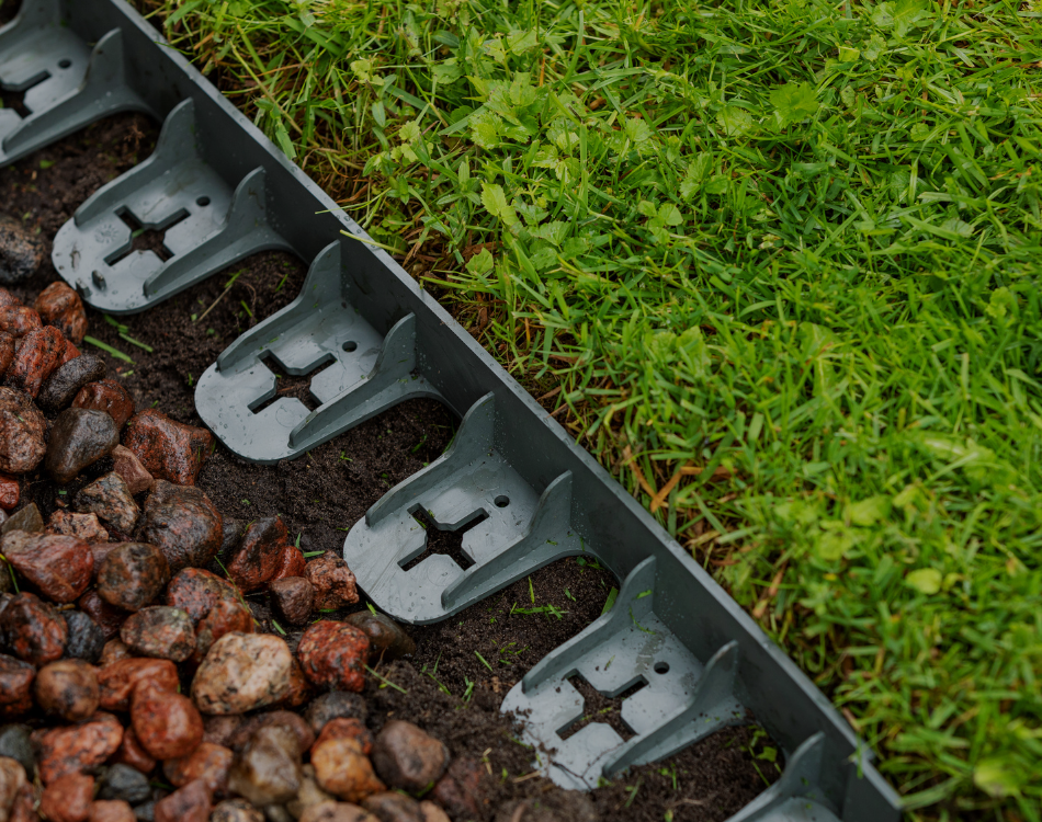 Closeup of black plastic landscape edging staked between gravel mulch and a grass lawn.
