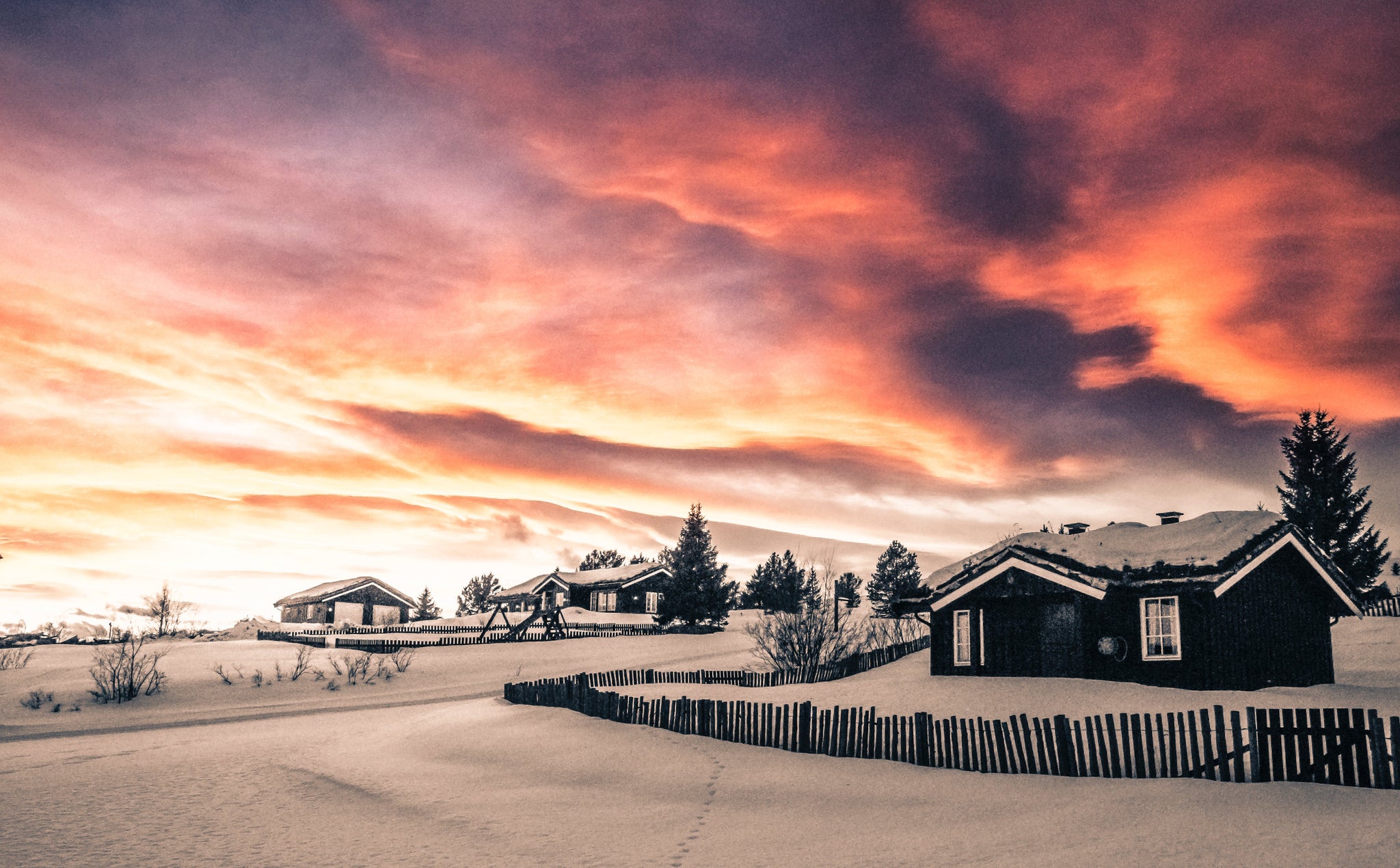 Snowy cabins at sunset, orange and purple sky.