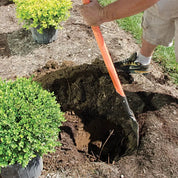 Gardener using Caprock irrigation shovel to dig a planting hole between landscape shrubs.