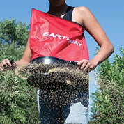 Gardener using Earthway bag spreader to broadcast seed across a lawn.