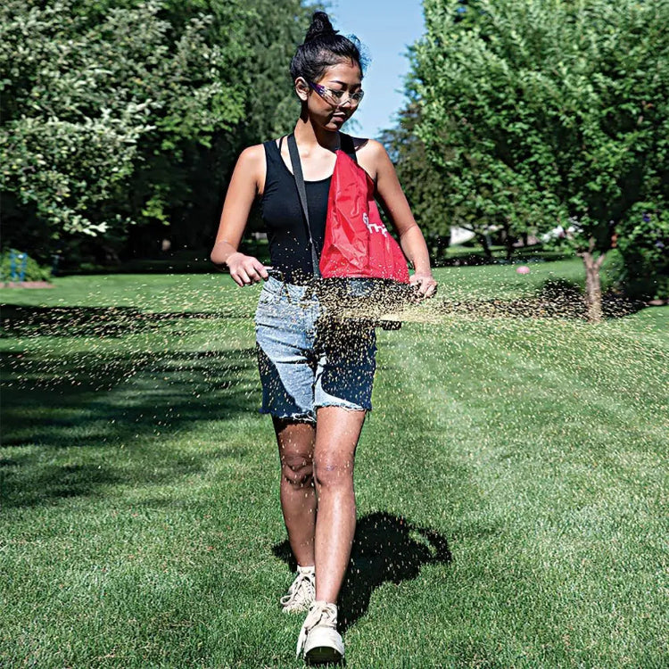 Gardener walking and broadcasting seed across a green lawn with Earthway shoulder spreader.