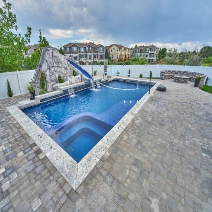 Inground pool with spa, rock waterfall, and slide; gray pavers.
