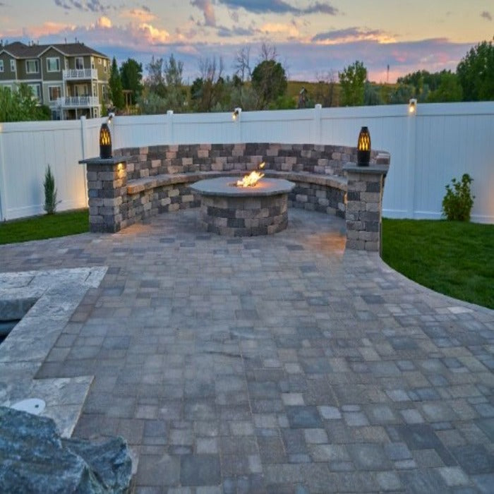 Stone fire pit and seating area at dusk, surrounded by a paved patio.
