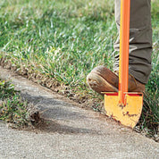 Person stepping on half-moon turf edger blade to cut sod along a concrete walkway.
