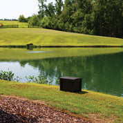Dark brown aeration system housing by a pond, nestled in a grassy landscape.
