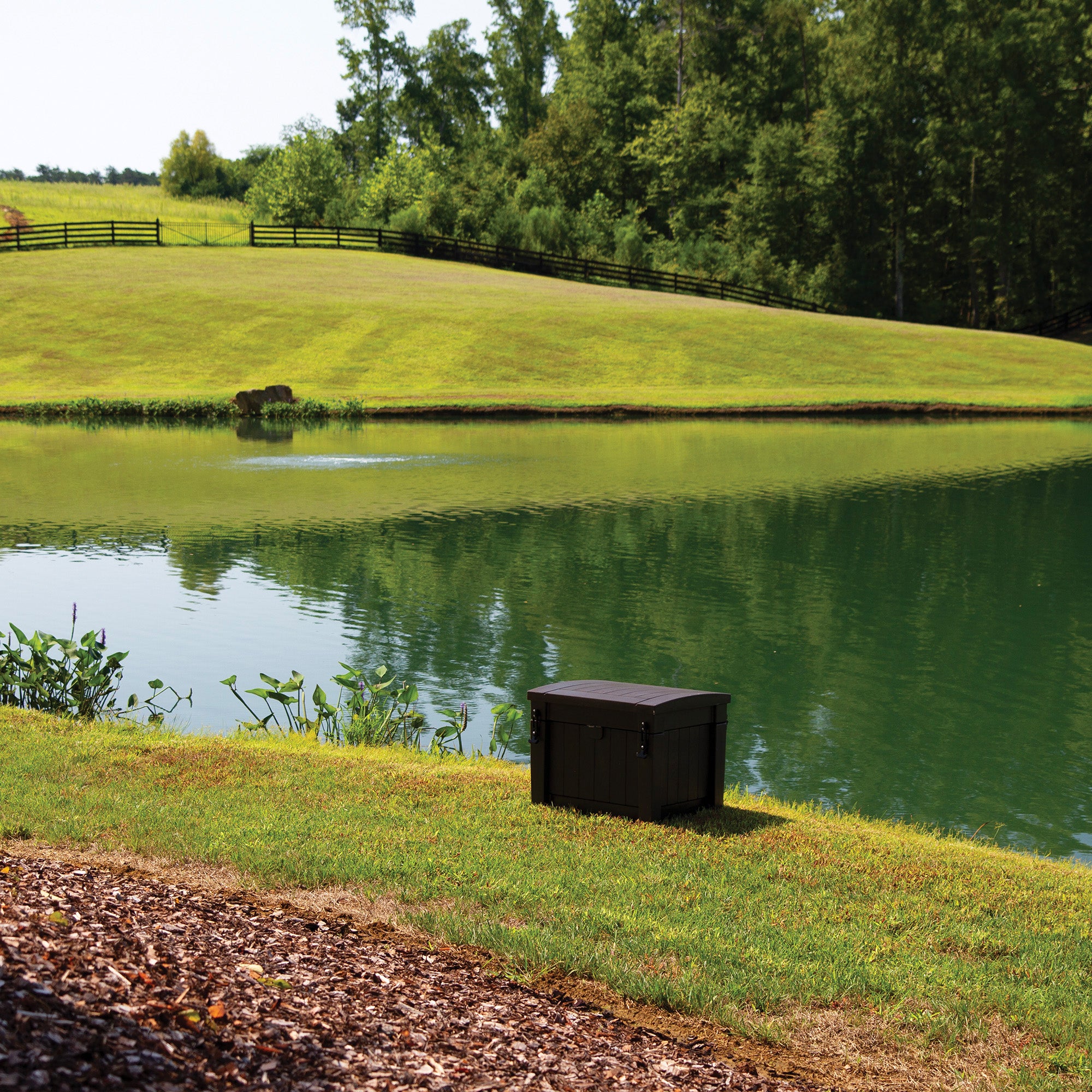 Dark brown aeration system housing by a pond, nestled in a grassy landscape.
