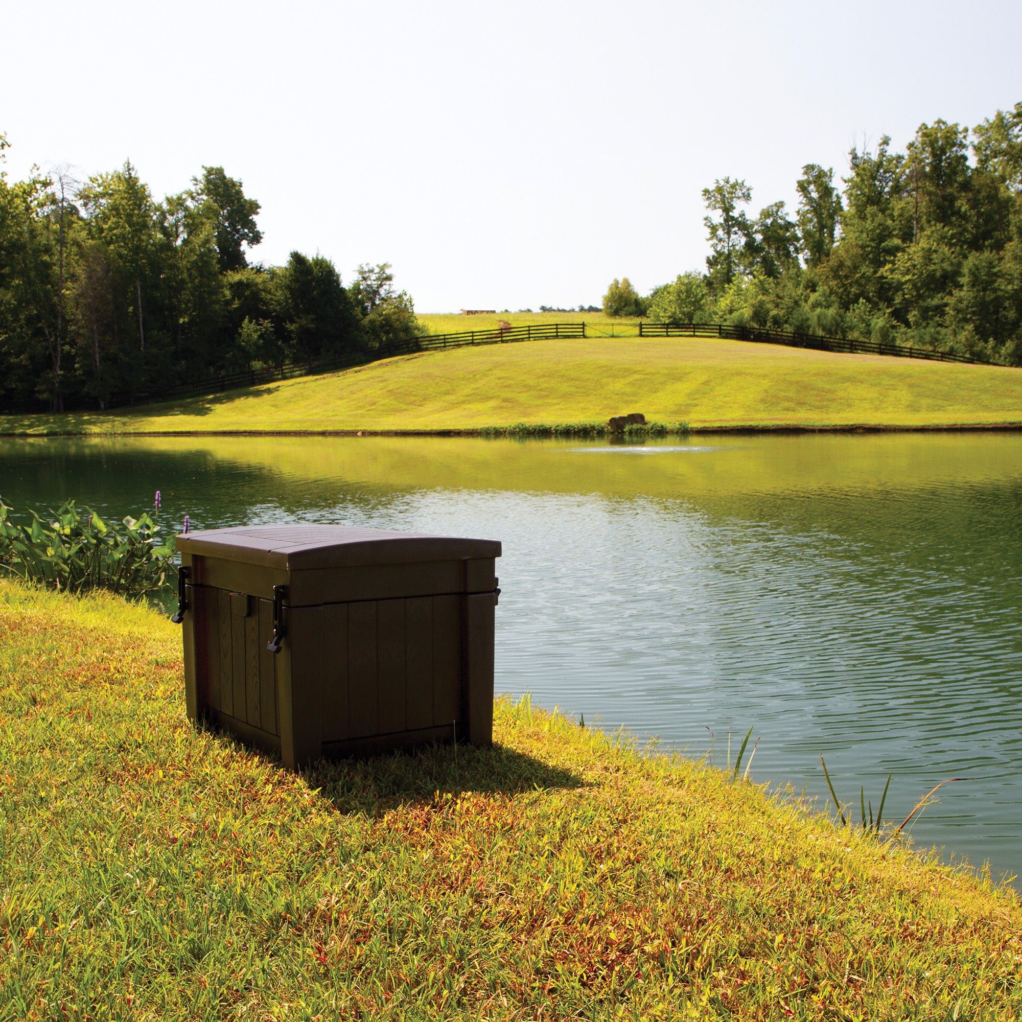 Dark brown aeration system unit by a pond, idyllic rural setting.
