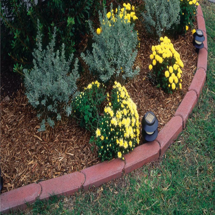 Red brick garden edging bordering yellow flowers and wood mulch.
