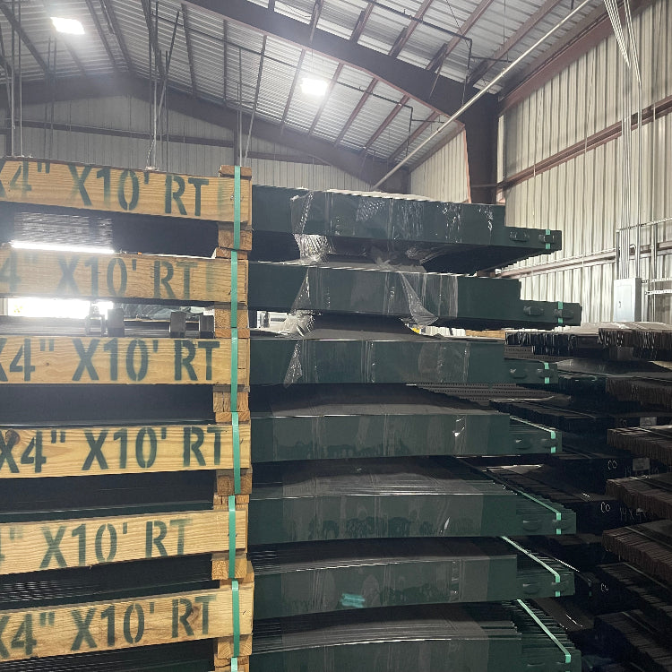 Pallet stacks of 4 inch by 10 foot green roll top edging in a warehouse storage bay.
