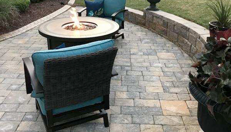 Cozy patio scene with fire pit and teal cushioned chairs on a gray brick paver patio.
