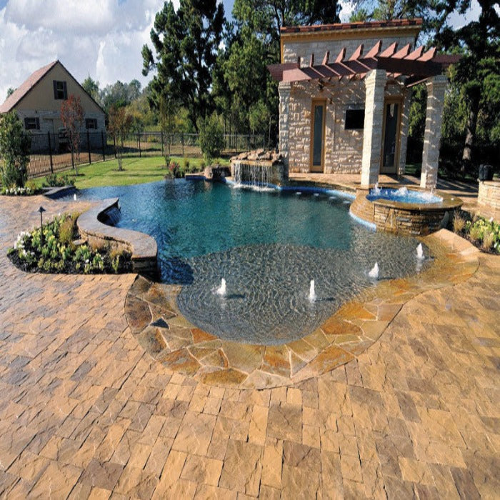 Luxury poolside patio with tan pavers and a tranquil water feature.
