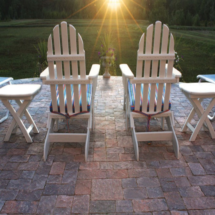 Patio chairs facing sunset over tranquil lawn, situated on a brick paver patio.
