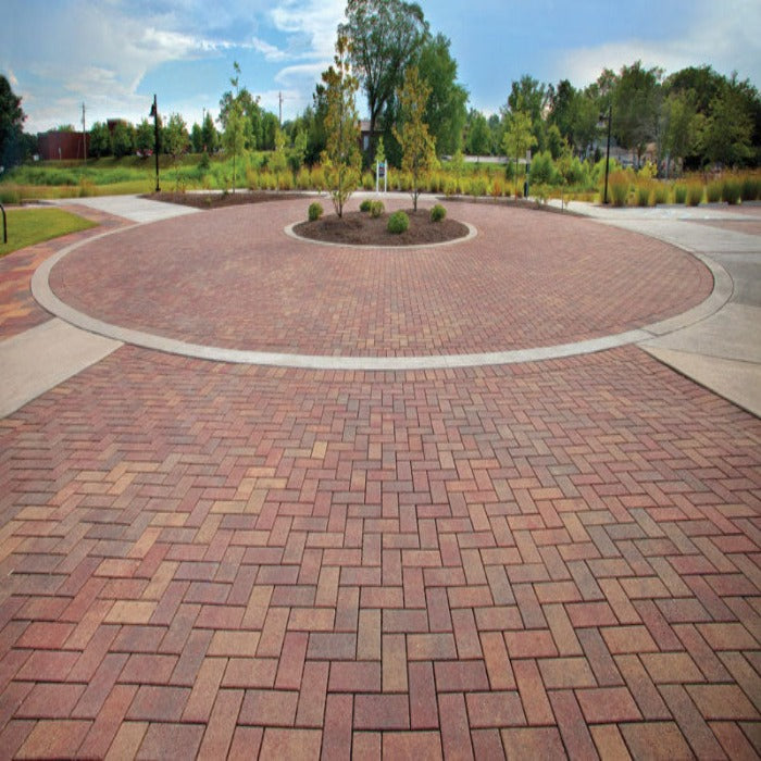 Red and brown brick pavers create a circular patio in a park-like setting.
