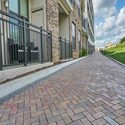 Multi-hued paving stones create a gently sloping driveway leading to an apartment building.
