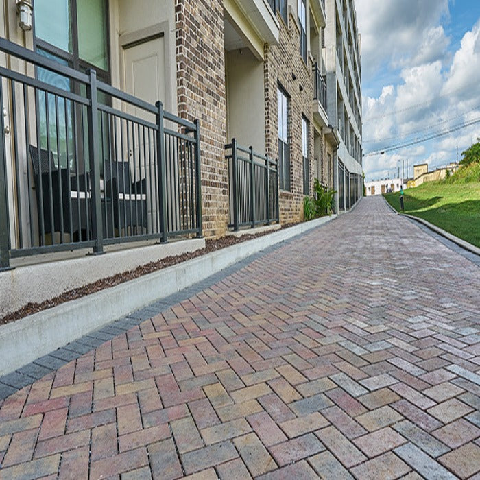 Multi-hued paving stones create a gently sloping driveway leading to an apartment building.
