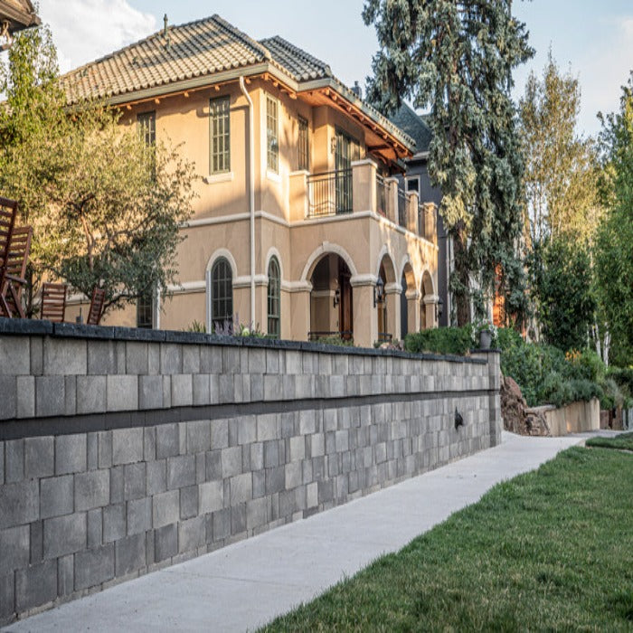 Contemporary gray stone wall blocks create a modern retaining wall, bordering a manicured lawn.
