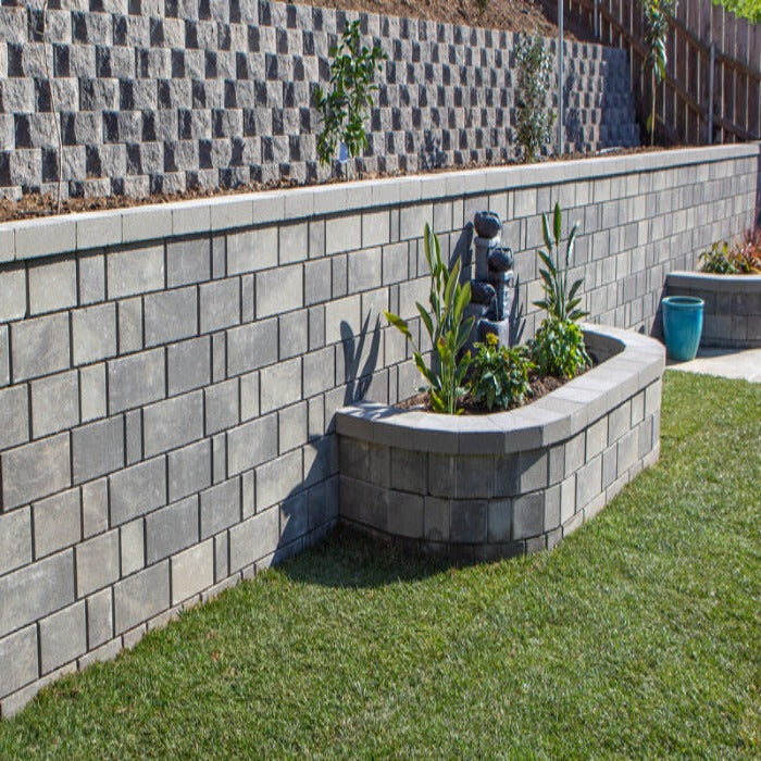 Gray retaining wall blocks create a tiered garden with a curved planter and small fountain.
