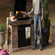 Outdoor kitchen with built-in grill, stone base, and man grilling.
