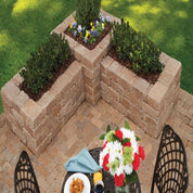 Tan brick retaining wall garden planter with flowers, creating a patio seating area.
