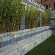 Contemporary retaining wall with integrated seating, illuminated at night, landscaped with ornamental grasses.
