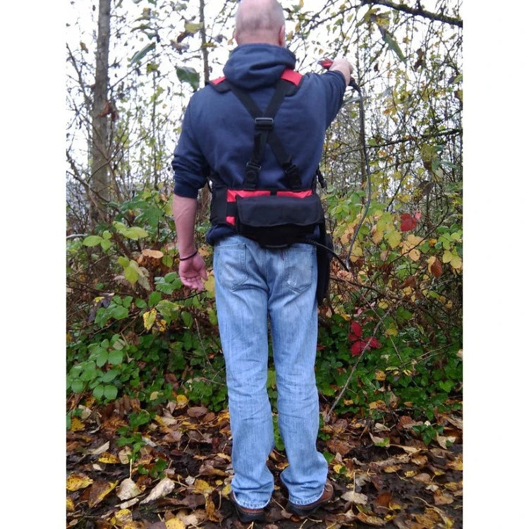 Person using cordless hand pruner outdoors, wearing a harness.
