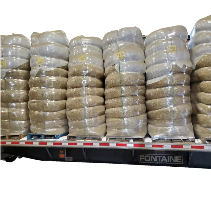 Large bales of straw wattles shrink-wrapped and secured on a flatbed trailer.
