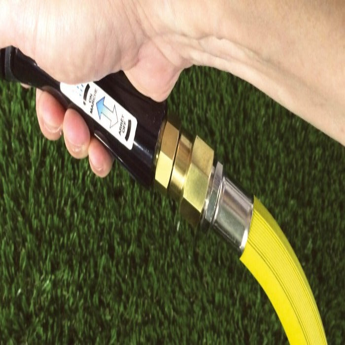 Brass hose swivel with on/off switch, connected to yellow hose, against green grass.

