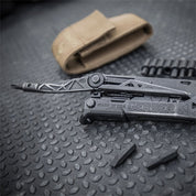 Black multi-tool with interchangeable bits, resting on a textured surface near a tan carrying case.
