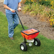 Person using a 50lb spreader on a lawn.
