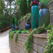 Regal Stone Pro Rockface retaining wall; elegant curved design, enhancing landscaping with lush greenery & large planters.
