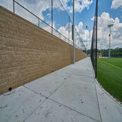 Tan concrete pathway beside a tan block retaining wall and sports field
