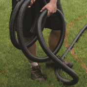 Person installing flexible black PVC pipe outdoors on a grassy lawn.

