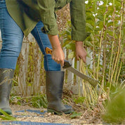 Person using a billhook to prune plants in a garden.
