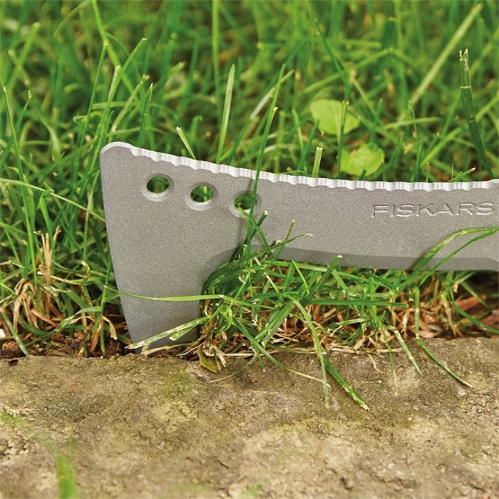 Silver billhook saw blade cutting through grass near ground.
