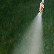 Brass nozzle spraying a fine mist over lush green grass.
