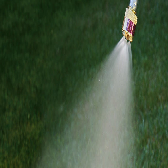 Brass nozzle spraying a fine mist over lush green grass.
