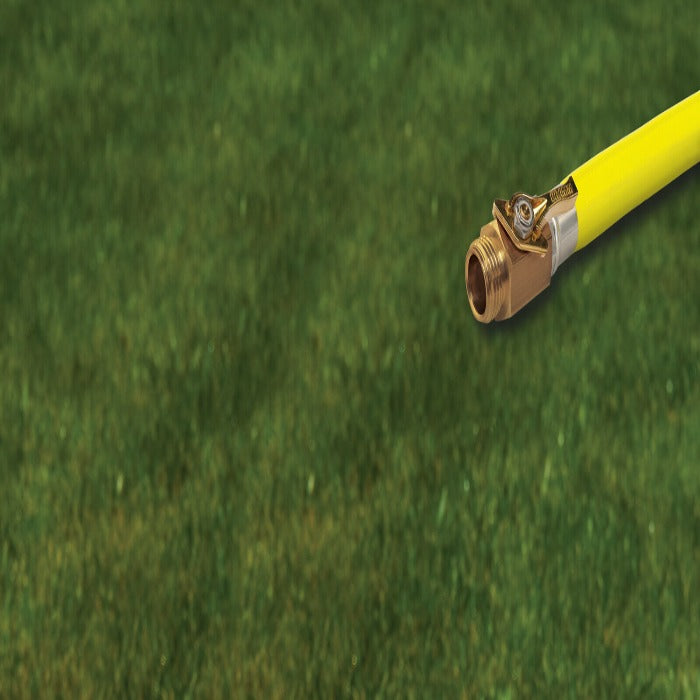 Brass shut-off valve attached to yellow hose, shown against a blurred green lawn background.
