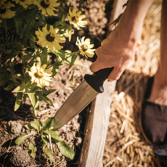 Stainless steel gardening knife used amongst yellow flowers in a garden bed.
