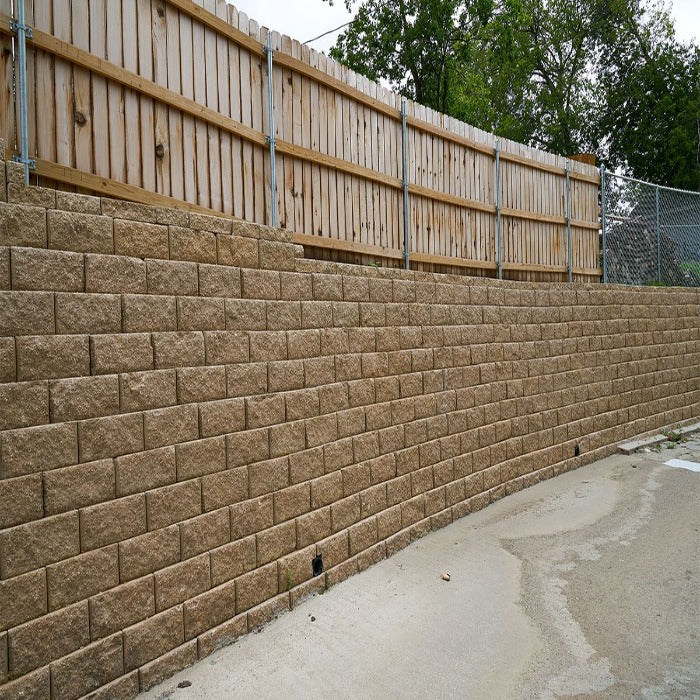Tan retaining wall blocks forming a curved wall, next to a wooden fence.
