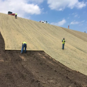 Workers installing straw erosion control blanket on a hillside.
